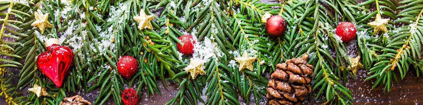 Fir tree branches spread out on wooden table, decorated with pine cones, red glass ornaments and gold star ornaments.